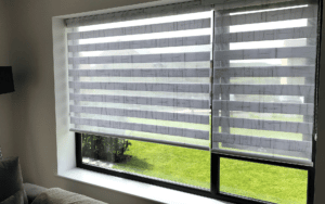 Photograph of a window with striped, half-open, blinds over it.
