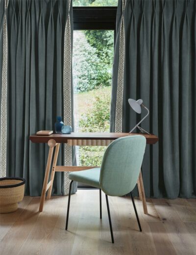 Photograph of a wooden table with a green chair and large grey curtains.