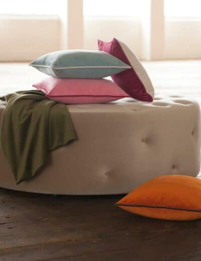 Photograph of a pile of colourful cushions on top of a pouffe stool.