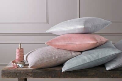 Photograph of a pile of grey and pink cushions on a table.